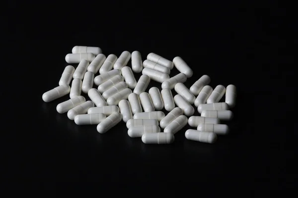 Pila de píldoras de medicina blanca sobre fondo negro —  Fotos de Stock