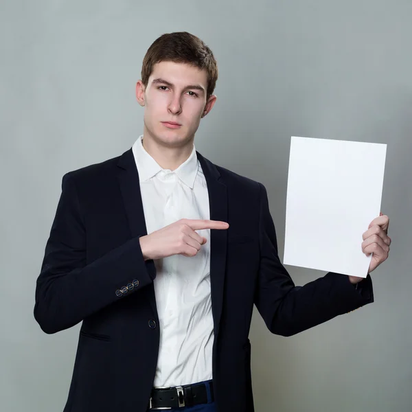Young business man with empty white paper on gray background — Stock Photo, Image