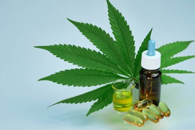 Kapsüllerdeki kenevir yağı CBD 'si ya da haplar ve şişe mavi arka plandaki yeşil marihuana yaprağının üzerinde duruyor. Alternatif tıp için kannabinoidlerin çıkarılması. Kozmetik