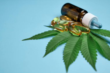 Kapsüllerdeki kenevir yağı CBD 'si ya da haplar ve şişe mavi arka plandaki yeşil marihuana yaprağının üzerinde duruyor. Alternatif tıp için kannabinoidlerin çıkarılması. Kozmetik
