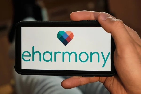 Eharmonie-Logo auf dem Bildschirm des Mobiltelefons in der Hand. Antrag auf Partnersuche und Bekanntschaft. Mann liegt auf dem Sofa und sucht Partner im Internet. Online-Dating. — Stockfoto