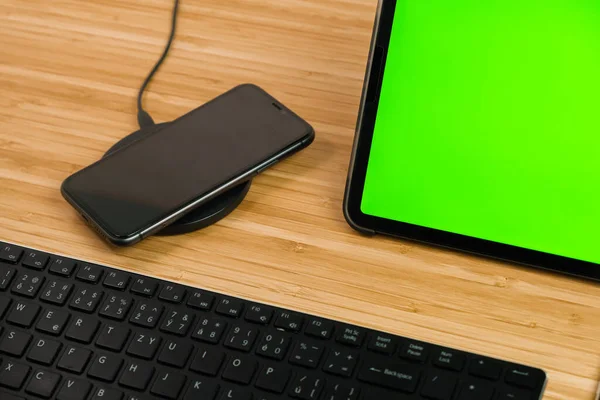 Smart phone ładuje się przy bezprzewodowym ładowaniu obok tabletu za pomocą klawisza chromo i klawiatury. — Zdjęcie stockowe