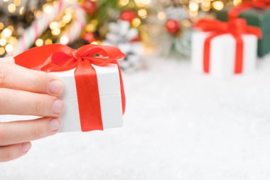 Kapalı kapılar ardında kırmızı kurdele olan beyaz hediye kutusunu tutan bir kadın. Şeker çubuğu, Noel ağacı ve fotokopi alanı olan altın ışıklar.