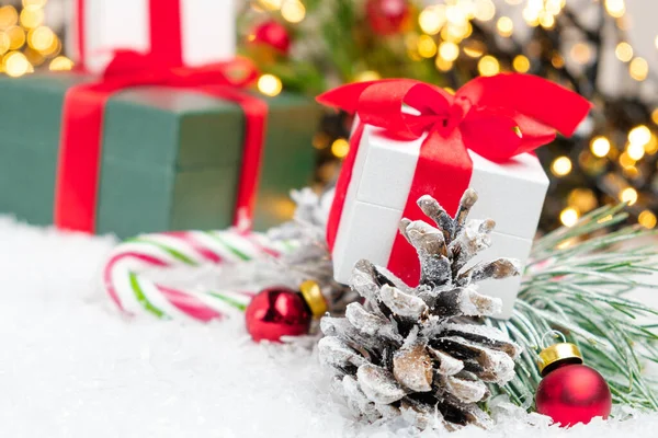 プレゼントやプレゼント、松のコーン、赤いボール、コピースペースを背景に金色のぼやけた光で雪の上にキャンディスティック. — ストック写真