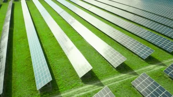 緑のフィールドに太陽電池パネルに沿って飛行します。グリーンエネルギーの生産のための太陽光発電所。太陽電池パネルにおける空の反射 — ストック動画