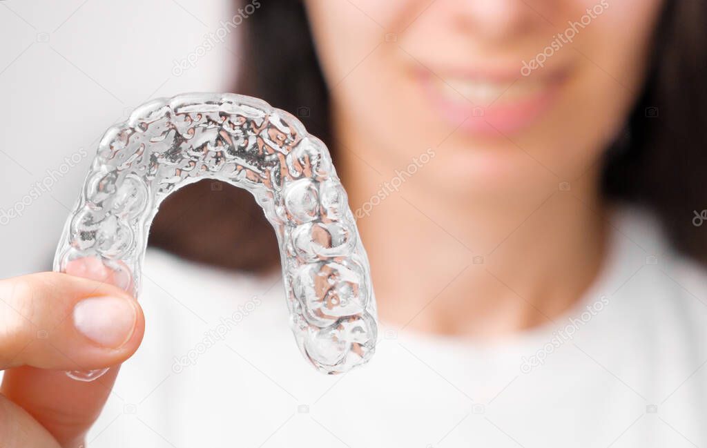 Close up orthodontic transparent aligner in womans hand. Removable braces.