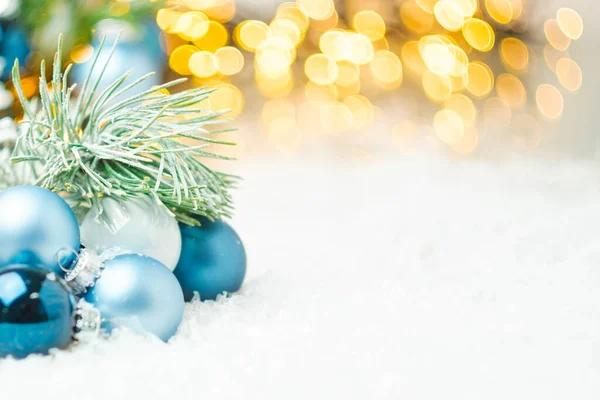 Bolas de Natal azuis e galho de pinho que coloca na neve no fundo da árvore de Natal e luzes douradas borradas com espaço de cópia. Preparação para a festa de Ano Novo. — Fotografia de Stock