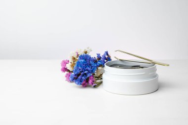 Beyaz masada üzerinde altın yamalar ve cımbız olan beyaz bir kutu. Renkli çiçekler ve fotokopi alanı. Cilt bakımı için kırışıklık önleyici bir kozmetik ürünü.
