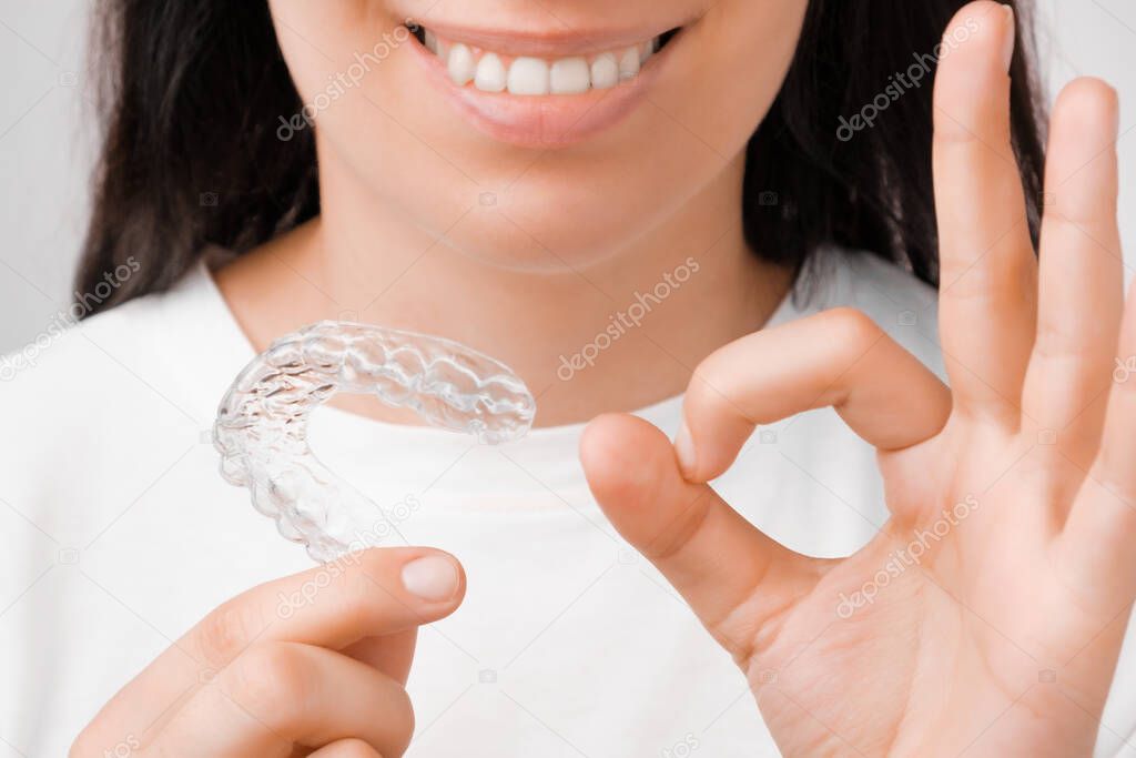 Woman shows sign ok and holding in the hand invisible aligner. Girl with a white smile using invisible whitening tray