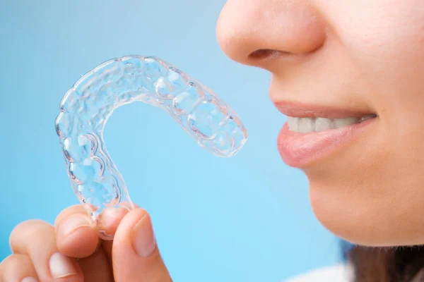 Feche a mulher segurando um aparelho removível transparente para um sorriso perfeito no fundo azul. Aligners ortodônticos para alisamento e clareamento dos dentes. — Fotografia de Stock