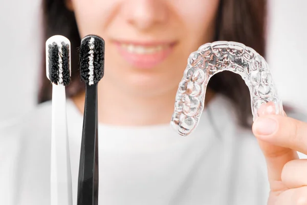 Schwarze und weiße Zahnbürsten und unsichtbare herausnehmbare Zahnspangen oder Zahnspangen in Frauenhänden — Stockfoto