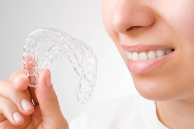 Plastik şeffaf diş telleri tutan neşeli genç bir kadın. Beyazlatma ve düzleştirme için ortodontik silikon hizalayıcı. 