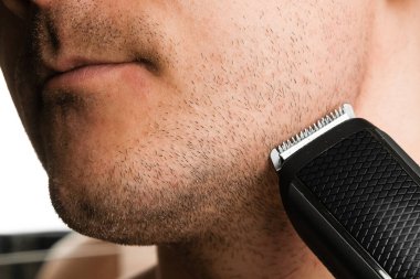 Adam sakalını elektrikli makasla kesiyor.