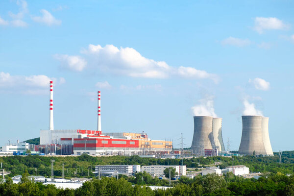 Panoramic view on nuclear power plant with steaming cooling towers on the background of blue sky.