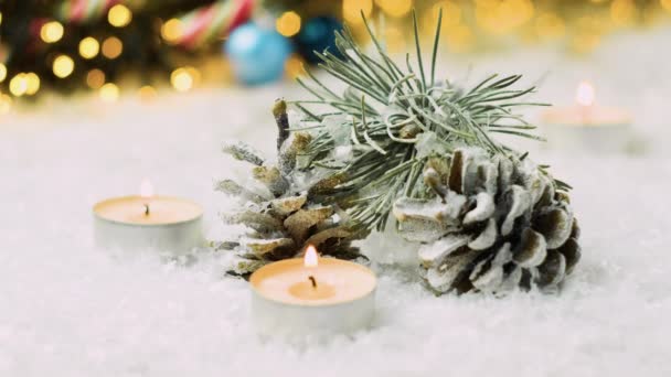 Spadający śnieg na szyszki sosnowe, gałąź jodły i świece na tle świąt Bożego Narodzenia. — Wideo stockowe