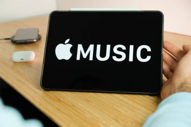 iPad tabletinin ekranındaki Apple müzik logosu kablosuz şarj cihazı ve hava podlarında şarj olan akıllı telefon iPhone ile arka planda, Kasım 2020, San Francisco, ABD.