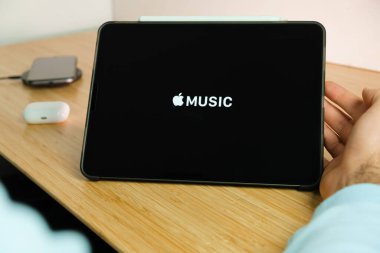 iPad tabletinin ekranındaki Apple müzik logosu kablosuz şarj cihazı ve hava podlarında şarj olan akıllı telefon iPhone ile arka planda, Kasım 2020, San Francisco, ABD.