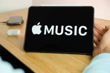 iPad tabletinin ekranındaki Apple müzik logosu kablosuz şarj cihazı ve hava podlarında şarj olan akıllı telefon iPhone ile arka planda, Kasım 2020, San Francisco, ABD