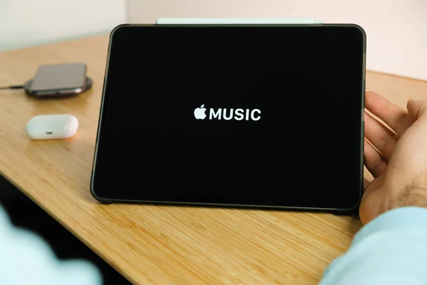 Logotipo de música de Apple en la pantalla de la tableta iPad con el teléfono inteligente iPhone de carga en el cargador inalámbrico y airpods en el caso en el fondo, noviembre 2020, San Francisco, EE.UU. — Foto de Stock
