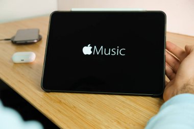 iPad tabletinin ekranındaki Apple müzik logosu kablosuz şarj cihazı ve hava podlarında şarj olan akıllı telefon iPhone ile arka planda, Kasım 2020, San Francisco, ABD