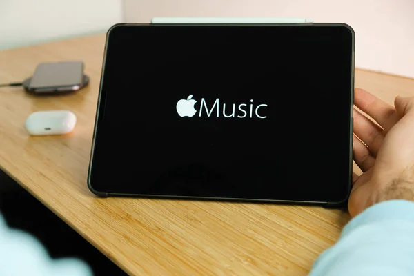 Logotipo de música de Apple en la pantalla de la tableta iPad con el teléfono inteligente iPhone de carga en el cargador inalámbrico y airpods en el caso en el fondo, noviembre 2020, San Francisco, EE.UU. — Foto de Stock