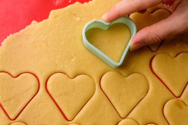  Kırmızı silikon hasırın üzerinde plastik kesici kullanarak kalpte zencefilli kurabiye yapmak. Sevgililer Günü için şekerler. 