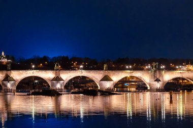 Panoramic view on Charles Bridge at night with reflection of lights in river Vltava, Prague, Czech Republic