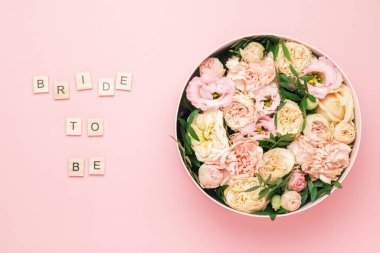 Gelin, ahşap karelere pembe arka planda harflerle kırmızı çiçekler ve güllerle dolu büyük yuvarlak bir kutuyla yazı yazacak..