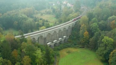 Trenin üst görüntüsü kemer köprüsünde hareket ediyor ağaçlarla çevrili..