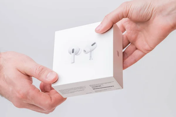 Man and woman hand holding a box with AirPods Pro on the grey background, December 2020, San Francisco, USA — Foto de Stock