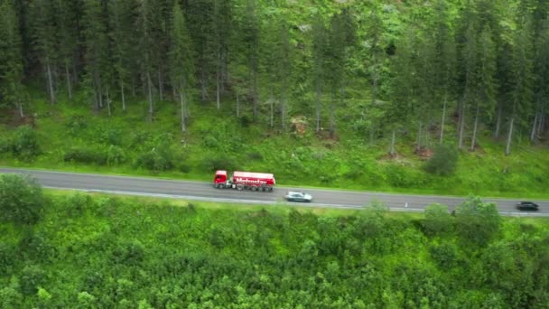 Zdjęcia lotnicze dużej czerwonej ciężarówki poruszającej się po drodze w lesie wśród wysokich zielonych drzew, wrzesień 2020, Słowacja — Wideo stockowe