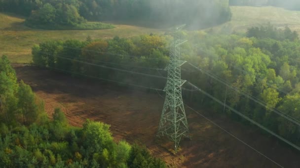 Gire alrededor de la torre de transmisión eléctrica de alto voltaje o pilón en el terreno a través de las nubes rodeadas de árboles a la luz del sol — Vídeo de stock