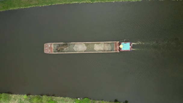 Вид с воздуха на большую грузовую баржу, движущуюся вдоль реки. Грузовой корабль или буксир, перевозящий песок или сырье. — стоковое видео