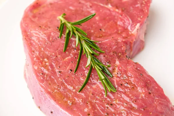 Rohes Rindersteak mit Rosmarinzweig und auf weißem Hintergrund isolierten Arten. — Stockfoto