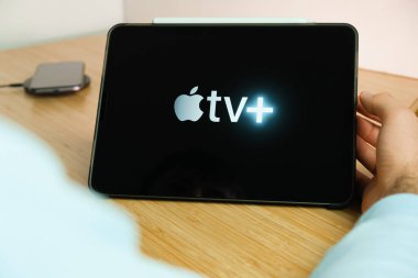 IPad tabletinin ekranında Apple TV logosu ve ahşap masadaki kablosuz şarjlı akıllı telefon, Kasım 2020, San Francisco, ABD