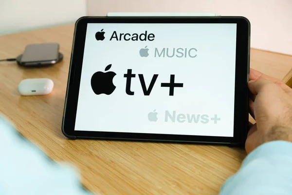 Apple Arcade, Musik-, Fernseh- und Nachrichtenlogo auf dem Bildschirm des iPad-Tablets mit dem Laden des Smartphones auf dem drahtlosen Ladegerät auf dem Holztisch, November 2020, San Francisco, USA — Stockfoto