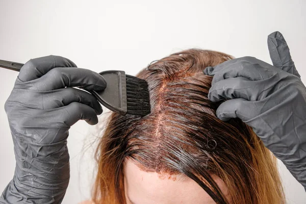 Donna che applica una tinta di colore ai capelli castani con un pennello. Tintura di radici grigie di capelli a casa. — Foto Stock