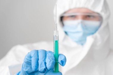 Doktor elinde koronavirüsün önlenmesi için şırıngada aşı, koruyucu maske ve koruyucu PPE giysi ve lastik eldiven.