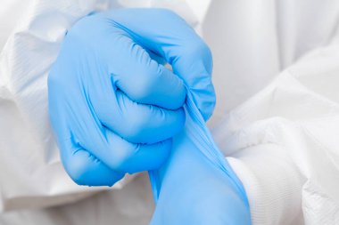 Korunaklı PPE giysisi giyen doktor ya da hemşire işe gitmeden önce koronavirüs hastası ya da test numuneleri ya da aşılama için lastik mavi eldiven takıyor.