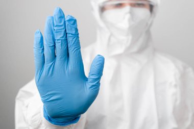 Koronavirüs, Sars-Cov-2 ve Covid-19 'a karşı koruyucu koruyucu PPE giysisi ve koruyucu yüz maskesi giyen doktor mavi lastik eldivenlerde işaret duruşu gösteriyor..