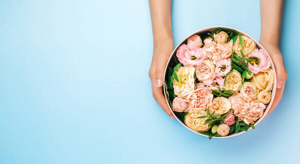 Florist holding a hat round box with floral composition on a blue background with copy space. Gift box for 8 March, St. Valentines Day, Mothers Day, birthday. wedding