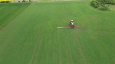 Tarım traktörünün tarlayı sürdüğü ve yeşil buğday tarlası püskürttüğü hava manzarası. Böcek ilacı, ot ilacı ya da böcek ilacı ile ekinlerin korunması