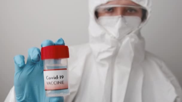 Lékař v ochranných oblecích, obličejové masce, bezpečnostních brýlích a gumových rukavicích demonstruje vakcínu proti koronaviru. Vývoj a testování vakcíny Covid 19 — Stock video
