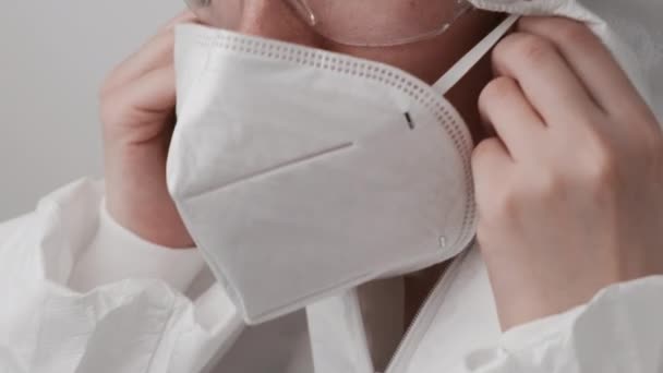 Εργαστηριακός υπάλληλος ή γιατρός που κουμπώνει μια στολή προστασίας από βιολογικούς κινδύνους και αναπνευστήρα FFP2 πριν από την εργασία με ασθενείς με κορωναϊό. — Αρχείο Βίντεο