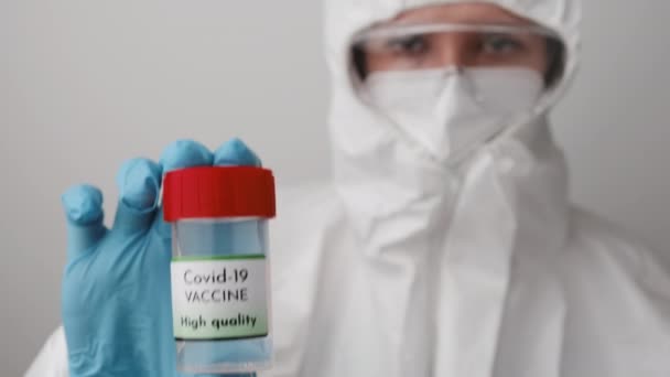 Качественная бутылка вакцины Covid 19 в руках врачей. Врач в защитном костюме, маске для лица, защитных гуглях и резиновых перчатках демонстрирует вакцину против коронавируса. — стоковое видео