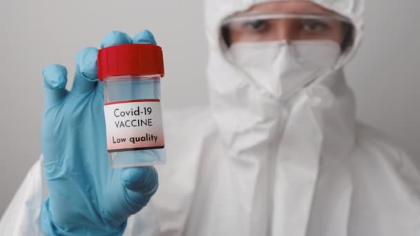 Lage kwaliteit Covid 19 vaccin fles in de hand van de arts. Dokter in beschermend pak, gezichtsmasker, veiligheidsgoogles en rubberen handschoenen demonstreren vaccin tegen coronavirus. — Stockvideo