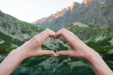 Elleriyle göl kenarındaki dağlara karşı kalp yapan kadınlar.. 