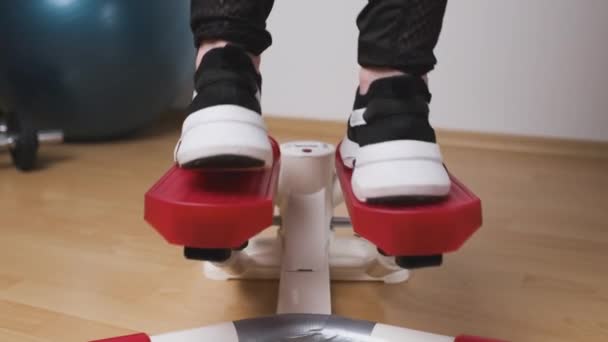 Achteraanzicht van vrouwelijke benen die oefeningen doen op de twist stepper in sneakers en sportkleding thuis tijdens lockdown. Workout thuis — Stockvideo