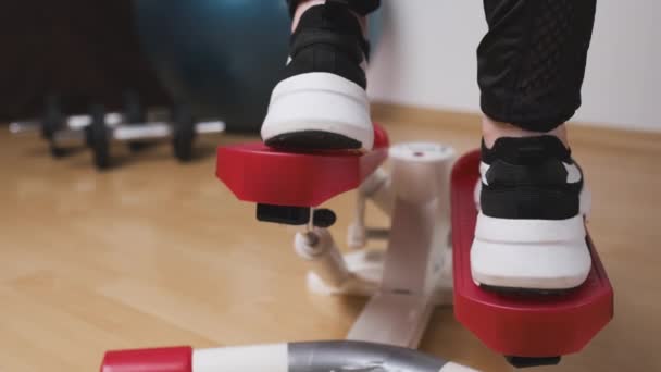 Achteraanzicht van vrouwelijke benen die oefeningen doen op de twist stepper in sneakers en sportkleding thuis tijdens lockdown. Workout thuis — Stockvideo