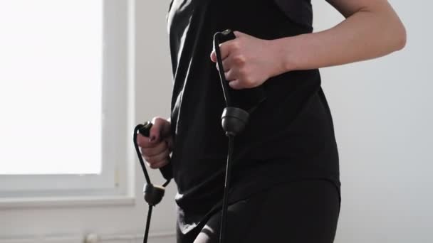 Vrouw in een zwarte sportkleding doet oefeningen met expander op de stepper. Cardio training thuis. Workout thuis tijdens lockdown — Stockvideo